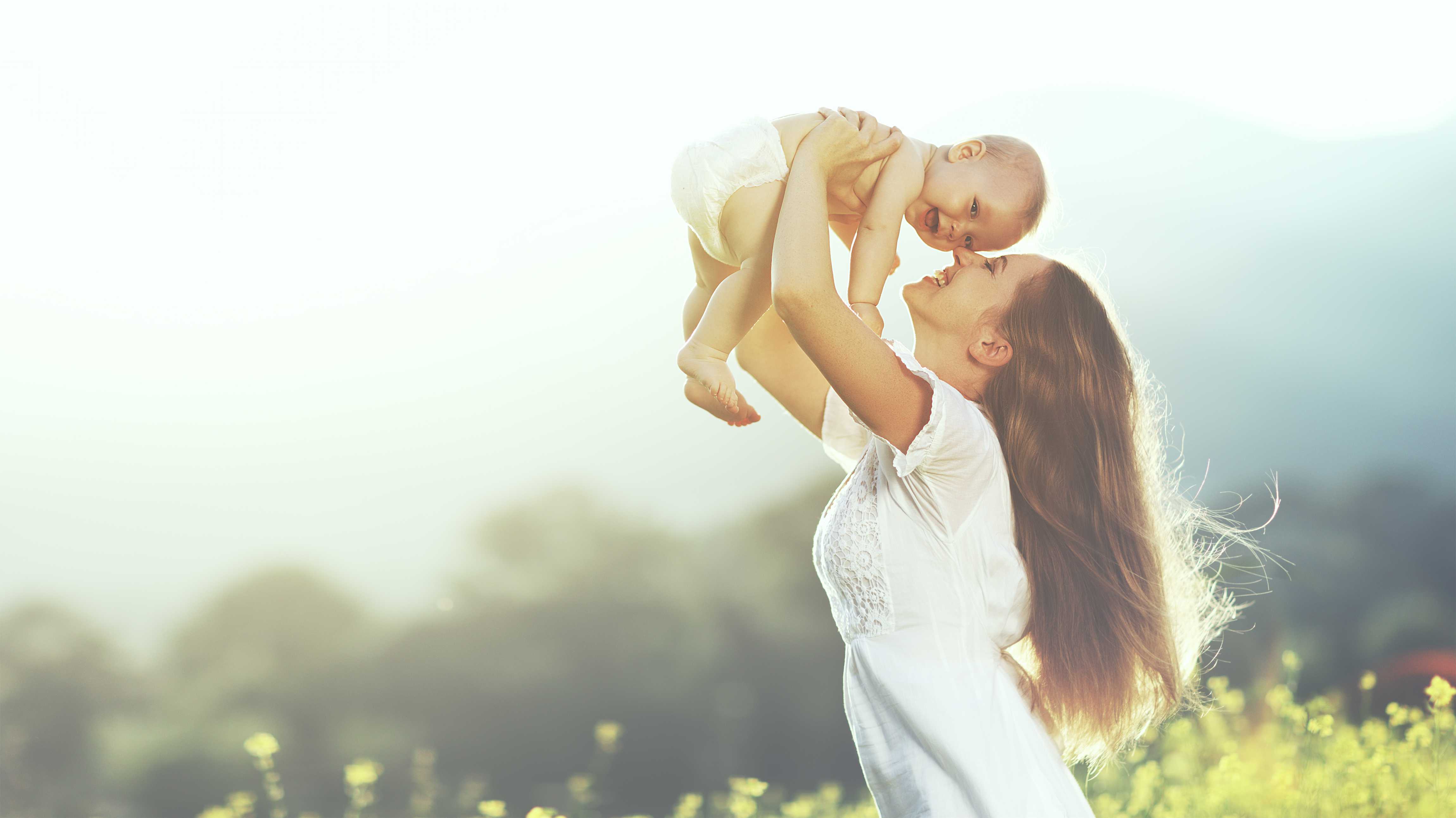 Mother lifting baby in a sunlit field